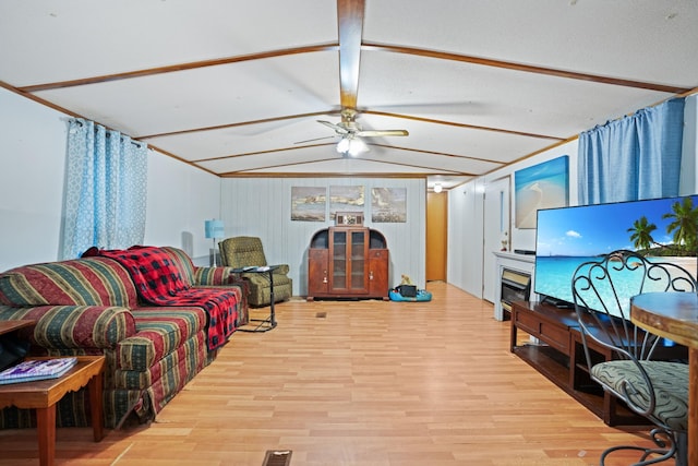 living room with vaulted ceiling with beams, ceiling fan, a fireplace, and light hardwood / wood-style flooring