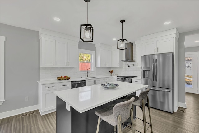 kitchen with white cabinets, a center island, wall chimney exhaust hood, and appliances with stainless steel finishes