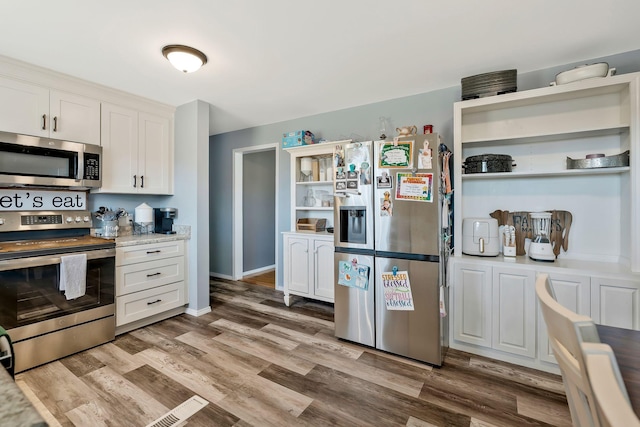 kitchen with light stone counters, white cabinetry, appliances with stainless steel finishes, light wood-type flooring, and open shelves