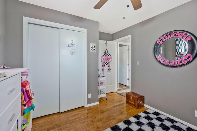 bedroom with a closet, wood finished floors, a ceiling fan, and baseboards