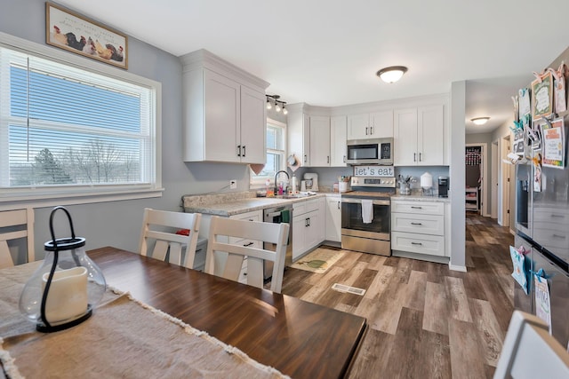 kitchen with light stone counters, a sink, white cabinetry, light wood-style floors, and appliances with stainless steel finishes