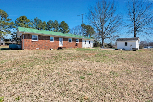 back of house featuring an outbuilding, metal roof, brick siding, crawl space, and a lawn