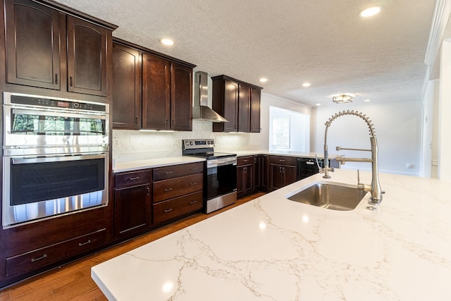 kitchen with sink, wall chimney exhaust hood, a textured ceiling, dark brown cabinets, and stainless steel appliances