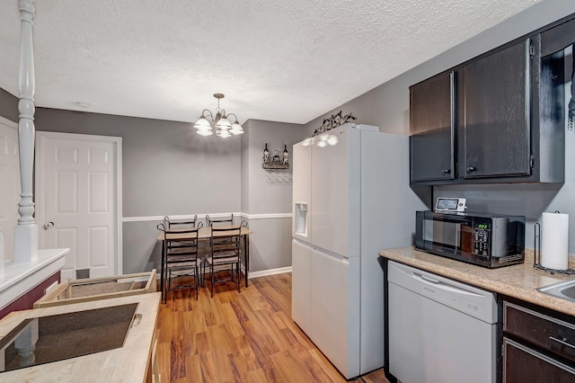 kitchen featuring hanging light fixtures, light hardwood / wood-style flooring, a chandelier, a textured ceiling, and white appliances