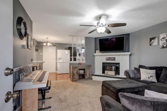 living room with a textured ceiling, light colored carpet, ceiling fan with notable chandelier, and a brick fireplace