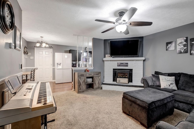 living room with carpet flooring, ceiling fan with notable chandelier, a textured ceiling, and a brick fireplace