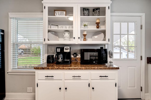 bar featuring a wealth of natural light, white cabinetry, and dark stone counters