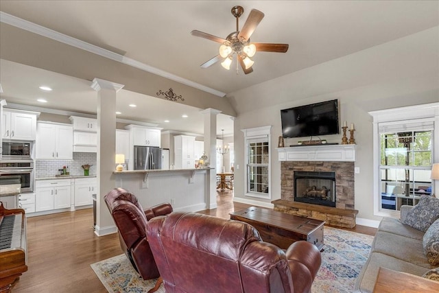 living room with light hardwood / wood-style flooring, a stone fireplace, ceiling fan, and ornamental molding