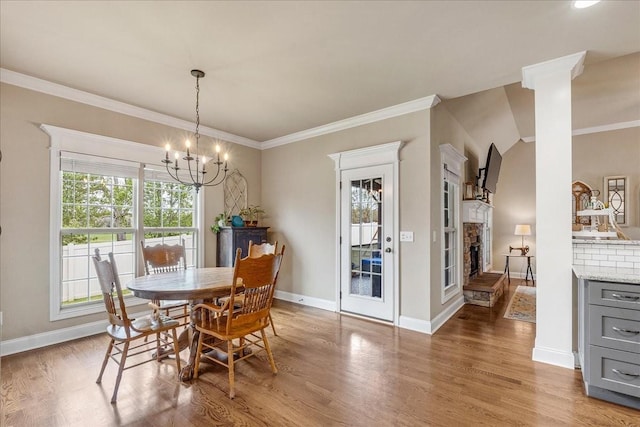 dining space with decorative columns, crown molding, a notable chandelier, hardwood / wood-style floors, and a stone fireplace