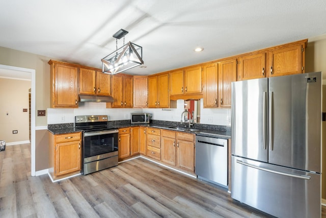 kitchen with sink, decorative light fixtures, light hardwood / wood-style flooring, appliances with stainless steel finishes, and decorative backsplash