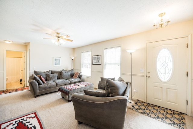 living room with a textured ceiling, light colored carpet, and ceiling fan with notable chandelier