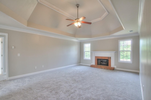 unfurnished living room featuring a raised ceiling, ornamental molding, a wealth of natural light, and a brick fireplace