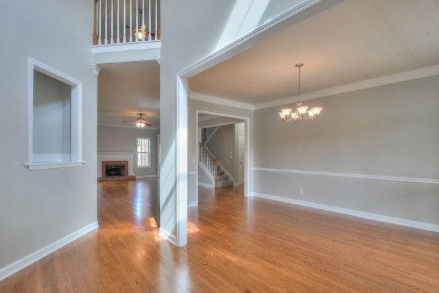 empty room featuring a fireplace, hardwood / wood-style floors, ceiling fan with notable chandelier, and ornamental molding