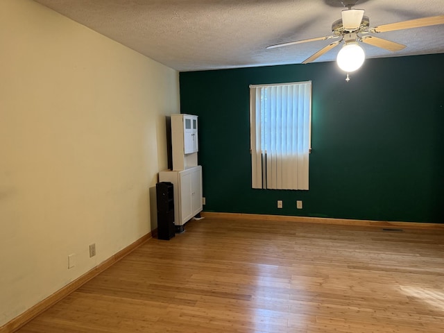 empty room with ceiling fan, light wood-type flooring, and a textured ceiling