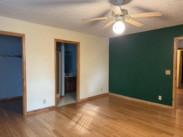 unfurnished bedroom featuring ceiling fan, ensuite bathroom, hardwood / wood-style floors, a walk in closet, and a closet