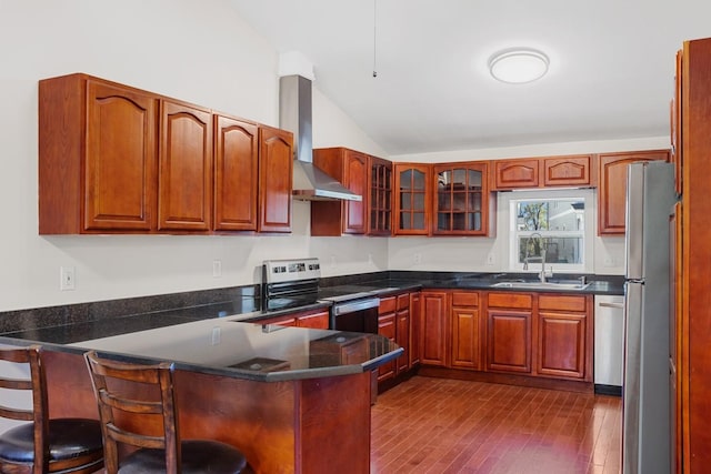 kitchen featuring a kitchen bar, appliances with stainless steel finishes, vaulted ceiling, sink, and wall chimney range hood