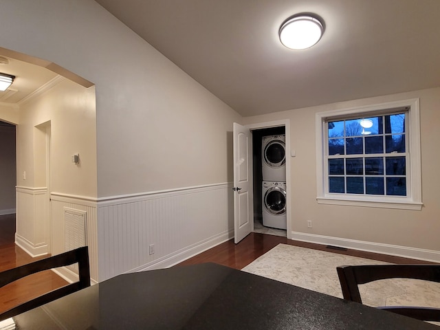 laundry room featuring crown molding, stacked washer and dryer, and dark wood-type flooring