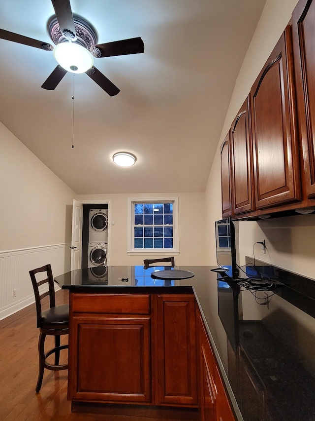 kitchen featuring ceiling fan, dark wood-type flooring, kitchen peninsula, stacked washer and dryer, and a kitchen bar