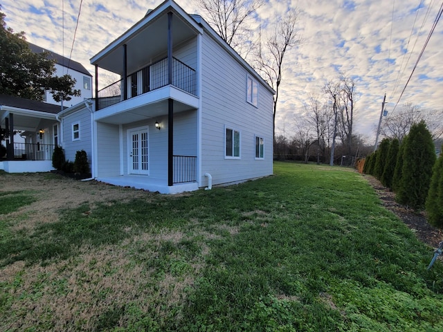 property exterior at dusk with a balcony, a yard, a patio, and french doors