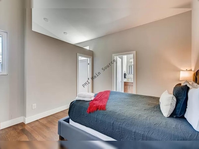 bedroom with ensuite bath, hardwood / wood-style floors, and vaulted ceiling