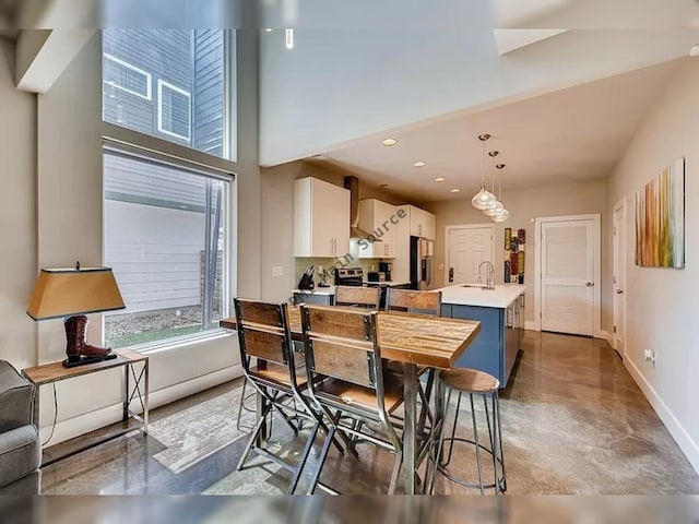 kitchen featuring a kitchen island with sink, decorative light fixtures, concrete flooring, a breakfast bar area, and stainless steel appliances