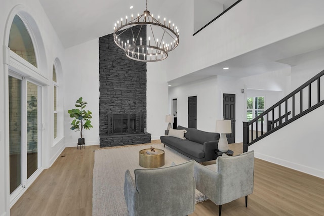 living room with a stone fireplace, hardwood / wood-style floors, a towering ceiling, and a chandelier