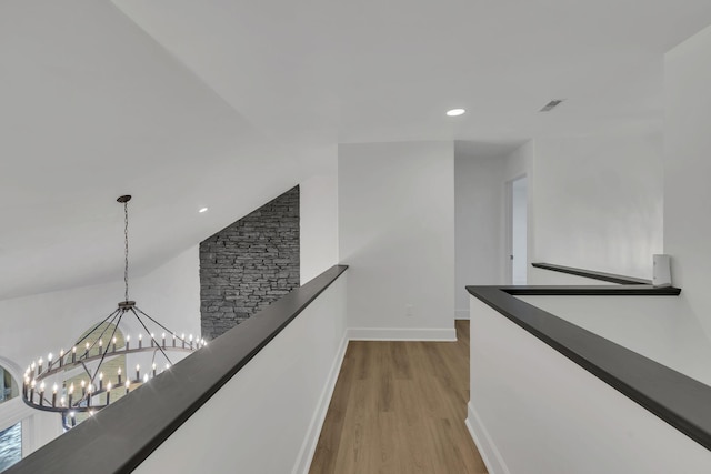 hallway featuring light hardwood / wood-style floors, vaulted ceiling, and a chandelier