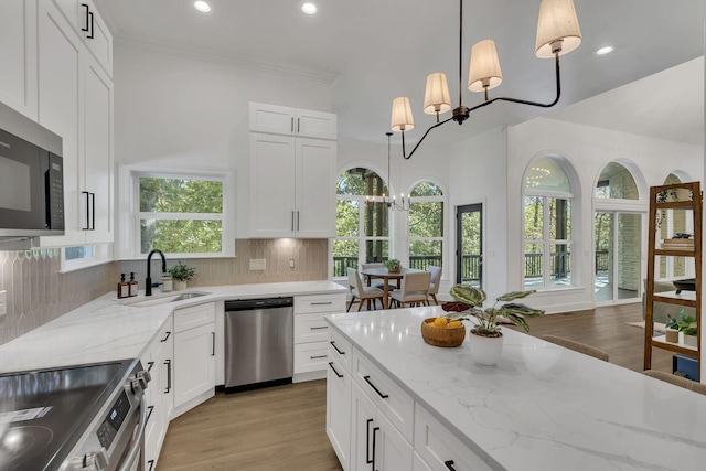 kitchen with appliances with stainless steel finishes, backsplash, sink, decorative light fixtures, and white cabinetry