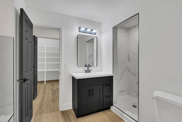 bathroom featuring a tile shower, vanity, wood-type flooring, and toilet