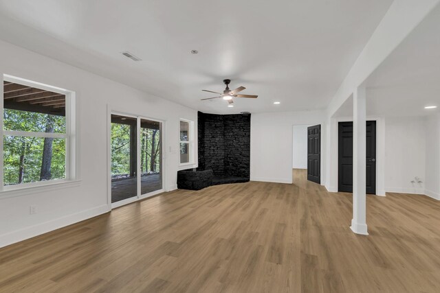 unfurnished living room featuring light hardwood / wood-style floors, a stone fireplace, and ceiling fan