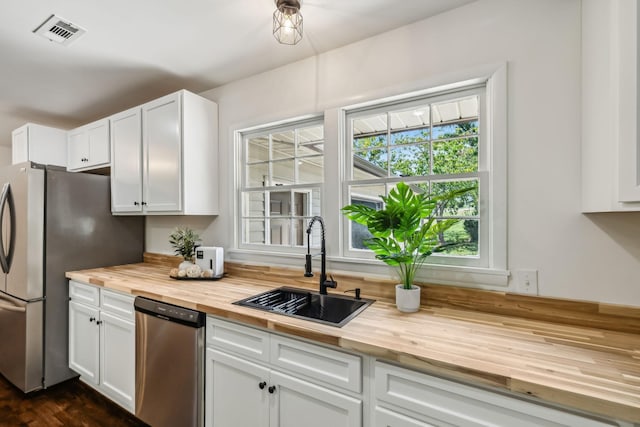 kitchen featuring wooden counters, appliances with stainless steel finishes, white cabinets, and sink