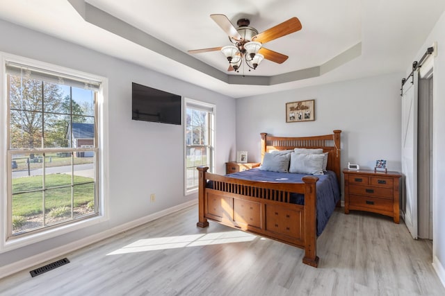 bedroom featuring ceiling fan, a barn door, a raised ceiling, and light wood-type flooring