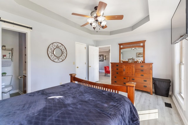 bedroom with a raised ceiling, ensuite bathroom, ceiling fan, and light hardwood / wood-style floors