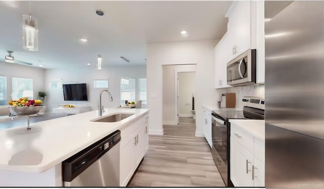 kitchen featuring sink, stainless steel appliances, light hardwood / wood-style floors, decorative light fixtures, and white cabinets