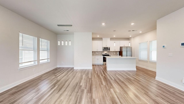 kitchen with a center island, white cabinets, light wood-type flooring, appliances with stainless steel finishes, and tasteful backsplash