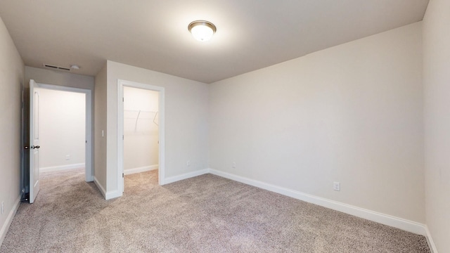 unfurnished bedroom featuring a walk in closet, light colored carpet, and a closet