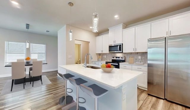 kitchen featuring appliances with stainless steel finishes, sink, decorative light fixtures, white cabinets, and an island with sink