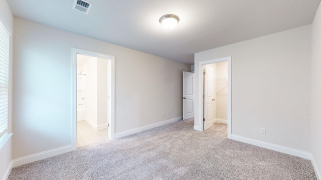 unfurnished bedroom with a walk in closet, light colored carpet, multiple windows, connected bathroom, and a closet