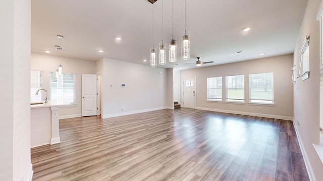 unfurnished living room with ceiling fan, sink, and light wood-type flooring