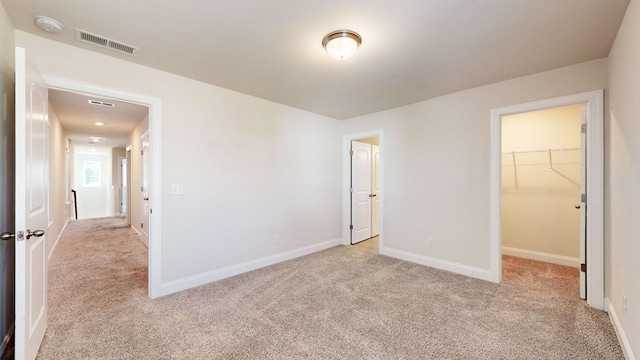 unfurnished bedroom featuring a spacious closet, a closet, and light carpet