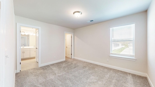 unfurnished bedroom featuring multiple windows, ensuite bathroom, and light carpet