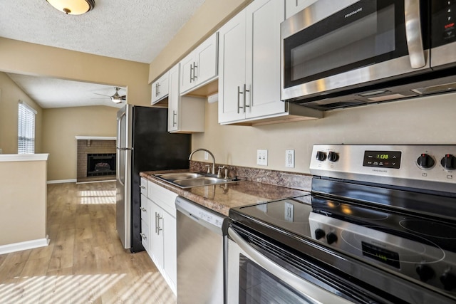 kitchen featuring sink, a brick fireplace, a textured ceiling, white cabinets, and appliances with stainless steel finishes