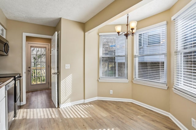 unfurnished dining area featuring a textured ceiling, light hardwood / wood-style floors, an inviting chandelier, and a wealth of natural light