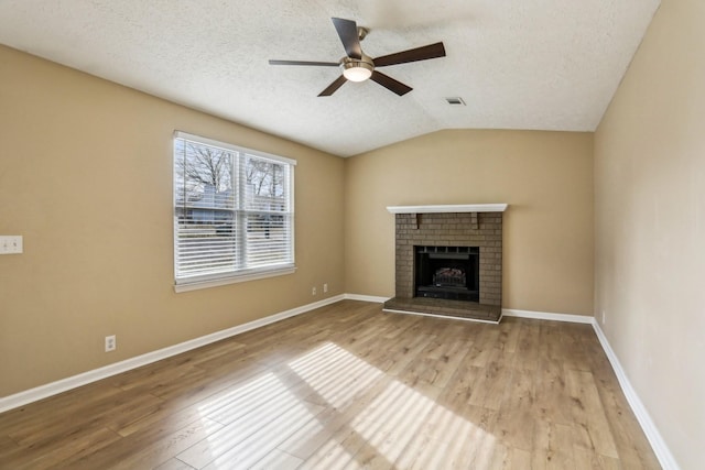 unfurnished living room featuring ceiling fan, a brick fireplace, light hardwood / wood-style floors, a textured ceiling, and vaulted ceiling