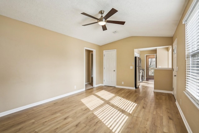 unfurnished bedroom with ceiling fan, stainless steel fridge, light hardwood / wood-style floors, lofted ceiling, and multiple windows