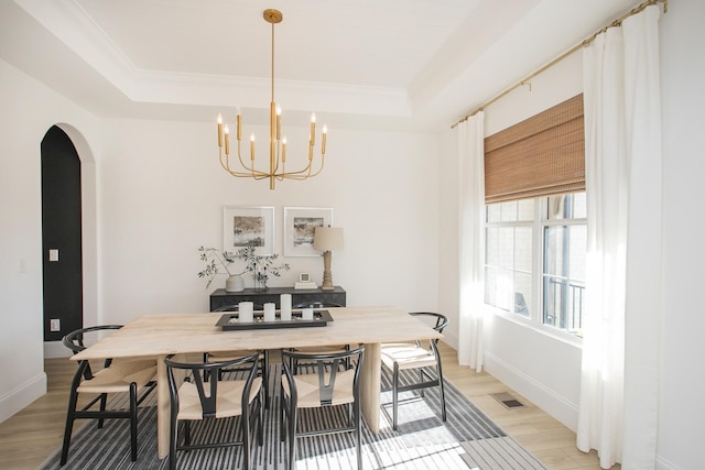 dining space featuring an inviting chandelier, a raised ceiling, light hardwood / wood-style floors, and crown molding