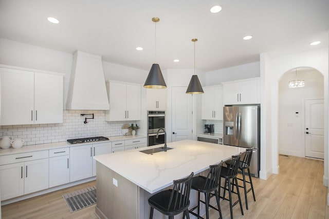 kitchen featuring white cabinets, custom range hood, stainless steel appliances, and a kitchen island with sink