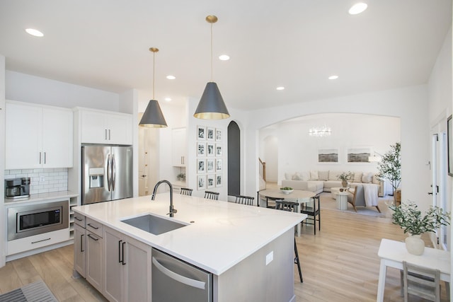 kitchen featuring a kitchen island with sink, sink, decorative light fixtures, white cabinetry, and stainless steel appliances