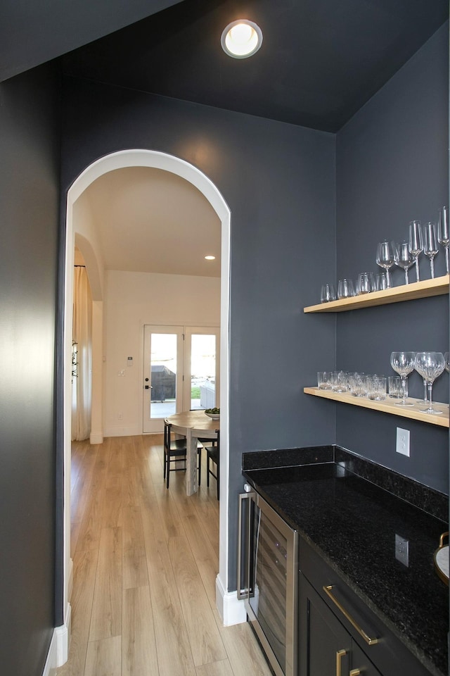 bar with dark stone countertops, beverage cooler, and light hardwood / wood-style flooring