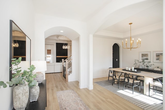 dining area with a chandelier, light wood-type flooring, a raised ceiling, and ornamental molding